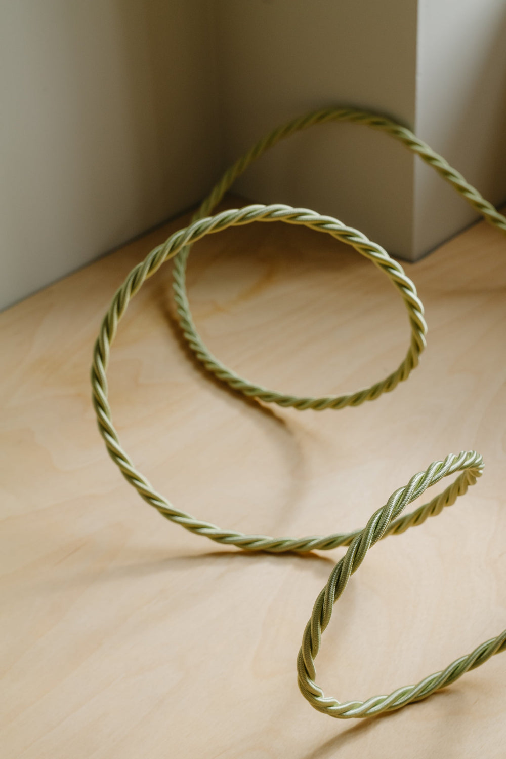 Coiled green rope on a wooden surface with a neutral background