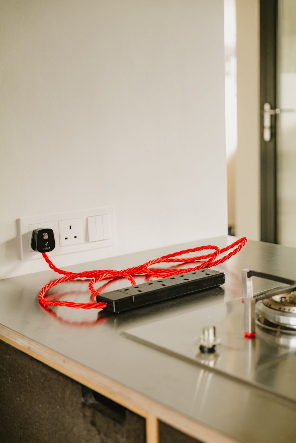 Red extension cord on a kitchen counter with a wall socket in the background